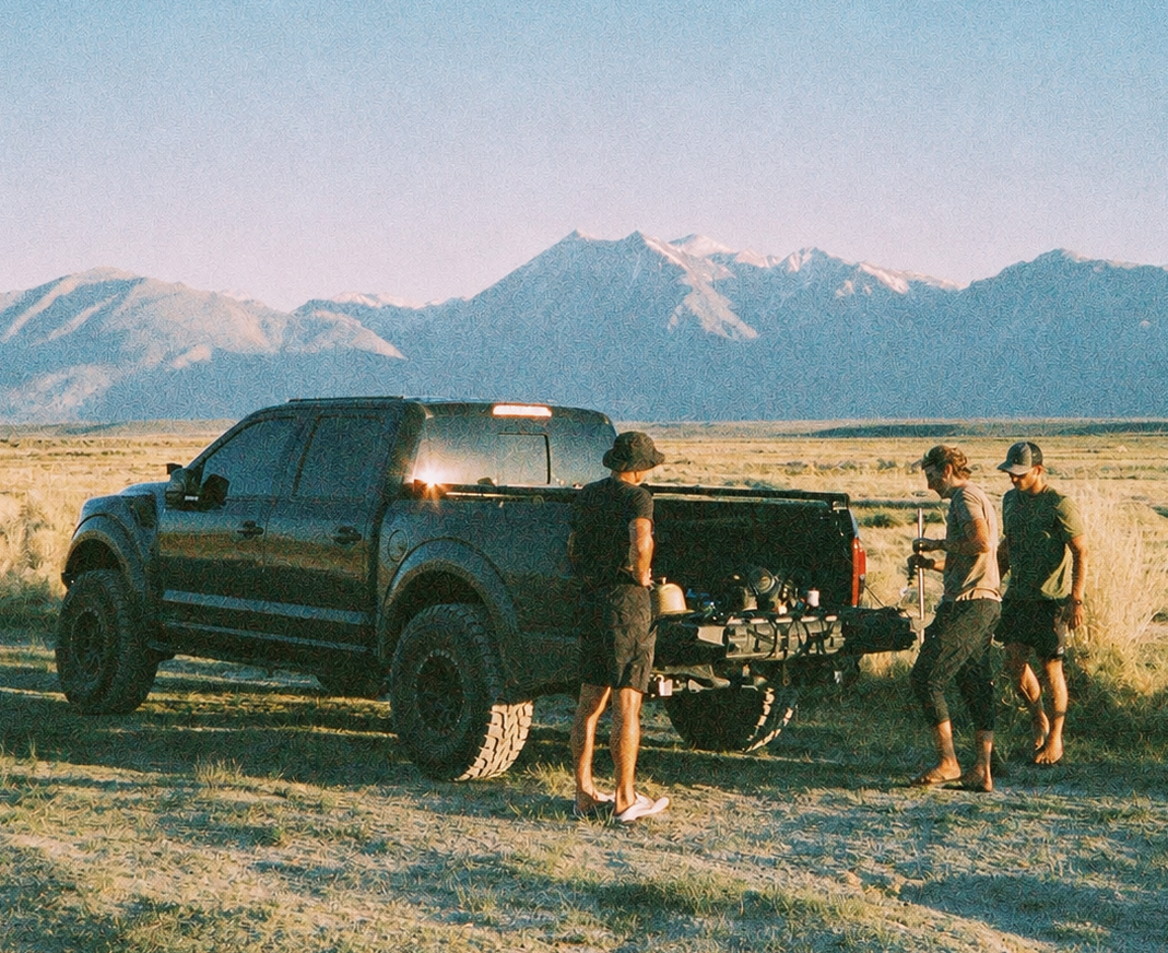 Men gathered around a truck in open country with mountains behind them
